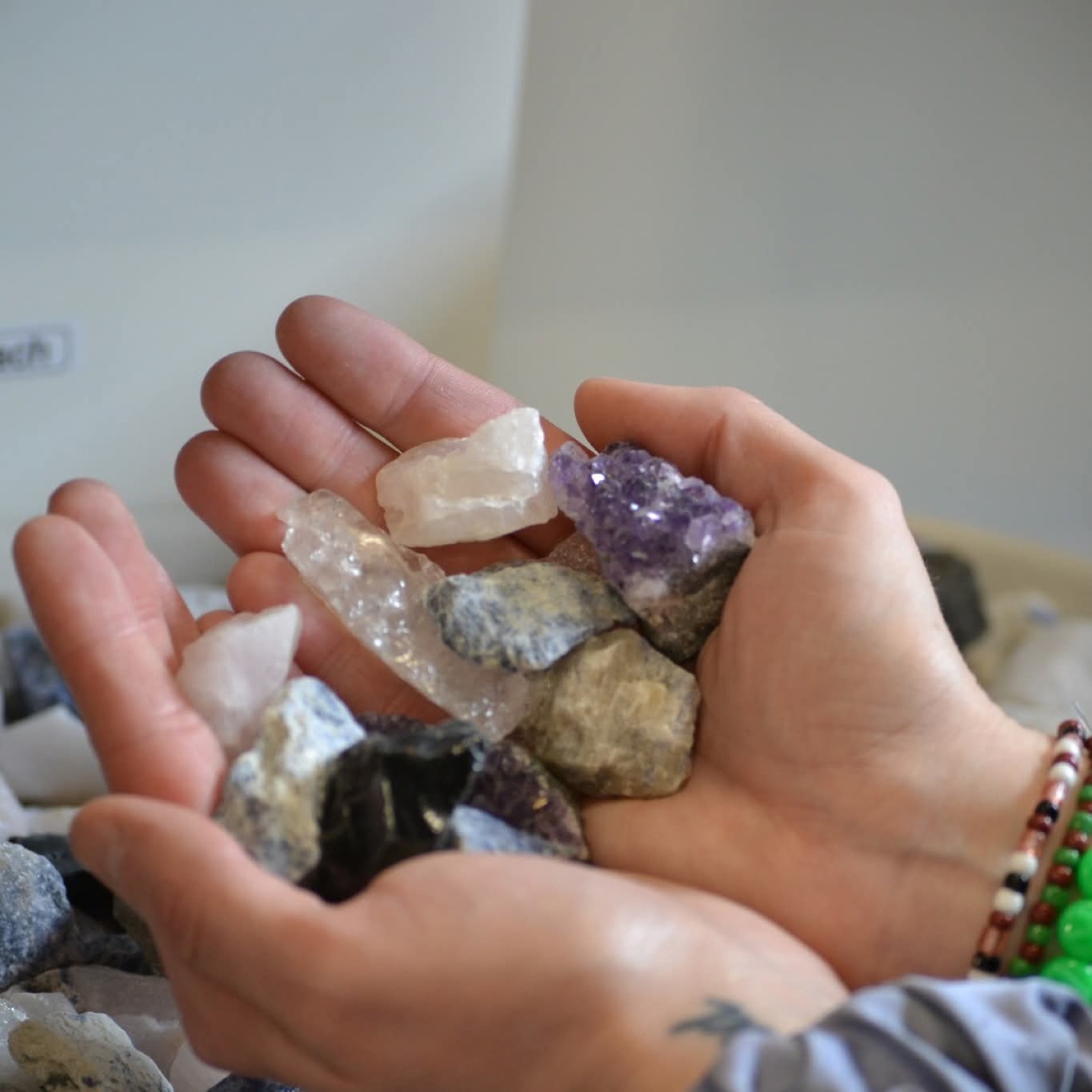 Two hands holding a selection of raw crystals including amethyst and quartz